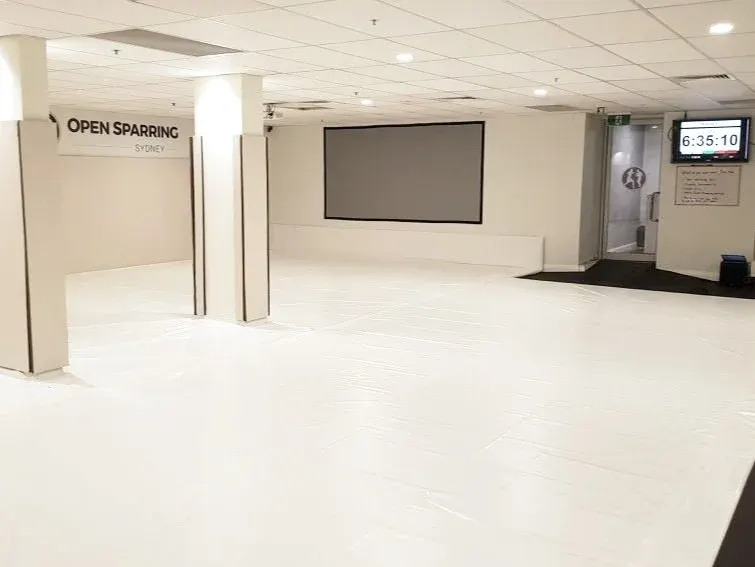 The Open Sparring floor — bright white mats, branded wall, Sydney CBD